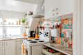 Bright kitchen with colorful tiled backsplash, white cabinets, a stove, and various kitchen utensils.