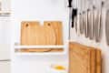Bamboo cutting boards with cat ears on a white shelf, alongside hanging kitchen knives and a bowl of lemons.