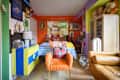 Colorful bedroom featuring a striped bedspread, orange armchair with a heart pillow, and eclectic wall art.