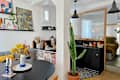 Cozy dining area with a round black table, yellow flowers in a vase, and a tall cactus. Open kitchen with black cabinetry and decor.