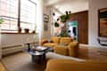 Cozy living room featuring mustard-colored curved sofas, a marble coffee table with a chess set, and large windows.