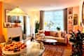 Cozy living room with a beige sectional sofa, colorful pillows, a round coffee table, and a fruit bowl centerpiece.