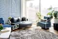 Modern living room with a blue patterned wall, circular leather sofa, plush rug, and plants, featuring a "GOOD VIBES" pillow.