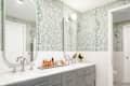 Modern bathroom with green dotted wallpaper, double sinks, silver faucets, and a tray of beauty products.