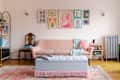 Cozy living room featuring a pink sofa, tufted ottoman, colorful wall art, and a patterned rug.