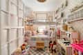 Cozy children's bedroom with a loft bed, plush toys, storage bins, and a play kitchen. Decorated with pastel colors and books.