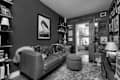 Cozy living room with a leather sofa, decorative pillows, a round ottoman, and framed artwork on the walls.