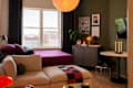 Cozy studio apartment featuring a purple bedspread, beige sectional sofa, and a round dining table with candles.