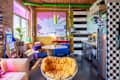 Brightly colored kitchen and dining area with a round table, blue chairs, yellow accent chair, and a large abstract painting.