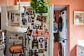 Refrigerator covered in photos, magnets, and notes, with a hanging plant and laundry appliances in the background.
