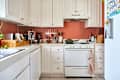 Cozy kitchen with white cabinets, a green pot on the stove, and various kitchen tools displayed on the wall.