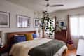 Cozy bedroom with a wooden bed, green throw blanket, large plant, and framed artwork on the walls.