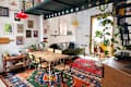 Cozy dining area with a wooden table, green chairs, colorful rug, and wall art, featuring plants and a bright red pendant light.