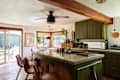 Modern kitchen with green cabinets, concrete countertops, wooden beams, and a dining area visible through sliding doors.