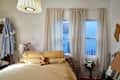 Cozy bedroom with a yellow bedspread, teddy bear, sheer curtains, and a small bouquet of flowers by the window.