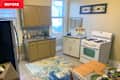 Kitchen with beige cabinets, stainless steel fridge, white stove, and a wooden dining table set for two with green plates.