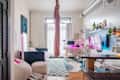 Cozy studio apartment featuring a bed, workspace with pink lighting, bean bags, and colorful rug.