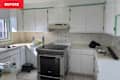 White kitchen with a stainless steel stove, beige countertops, and floral tile backsplash; items on the counter include a water bottle and cleaning cloth.
