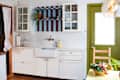 Bright kitchen with white cabinets, colorful striped shelves, a farmhouse sink, and a bowl of vegetables on the table.