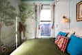 Cozy bedroom with green bedding, colorful pillows, a mural of trees, and a window with light curtains.