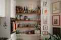Cozy kitchen corner with wooden shelves displaying glassware, plants, and decorative items, alongside a stove and fridge.
