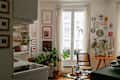 Cozy kitchen corner with a glass-top table, plants, framed art, and a window with sheer curtains.