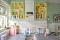 Colorful kitchen with open shelves displaying glassware, plates, and decorative items, alongside a sink and cutting boards.