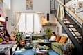 Cozy living room with a green sectional sofa, a woman using a laptop, an arcade game, and colorful decor.