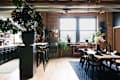 Spacious dining area with a large wooden table, black chairs, and various plants, featuring a bar counter and large windows.
