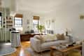 Cozy living room with a light sofa, wooden coffee table, and decorative plants, featuring a kitchen area with striped walls.