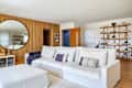 Bright living room featuring a white sectional sofa with decorative pillows, a round mirror, and wooden shelving with decor.