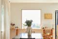 Dining area featuring a large vase with flowers on a black table, framed photos, and a window with natural light.