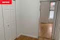 A small room with white walls, two closet doors, and light wooden flooring, leading to another room with windows.