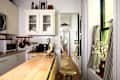 Cozy kitchen with wooden island, white cabinets, coffee maker, and a view into a bright hallway with floral decor.
