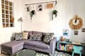 Cozy living room with a purple sectional sofa, decorative pillows, a green coffee table, and playful wall decor.