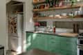 Modern kitchen with green cabinets, open wooden shelves, a white fridge, and a stainless steel countertop.