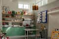 Bright kitchen with green cabinets, stainless steel appliances, wooden shelves, and colorful artwork on the walls.