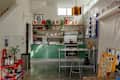 Bright kitchen with green cabinets, stainless steel appliances, a bar cart, and colorful wall art.