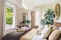 Cozy bedroom featuring a bed with layered blankets, decorative pillows, a woven tray with tea, and a large window with greenery outside.