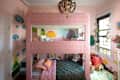 Bunk bed with pink patterned fabric, colorful wall murals, plush toys, and a cozy reading nook in a children's room.