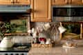 A cozy kitchen scene featuring a vintage kettle, decorative paintings, utensils in a basket, and cookies under a glass dome.