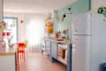 Bright kitchen with pastel blue cabinets, a retro fridge, colorful decor, and a round table with yellow and red chairs.