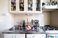 Compact kitchen with stainless steel sink, drying rack, coffee maker, and gas stove, featuring colorful dishes and utensils.