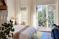 Bright bedroom with a white bedspread, a lamp, and a balcony door leading to a green outdoor space.