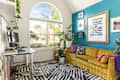 Cozy corner with a yellow striped sofa, colorful pillows, a glass desk, and large window with greenery outside.