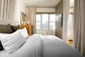 Cozy bedroom featuring a bed with white and olive green pillows, a wooden dresser, and large windows with sheer curtains.