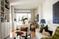 Bright living room featuring a white sofa, wooden bookshelves, and a round table with floral arrangements.