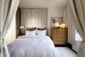 Cozy bedroom featuring a light bedspread, green accent pillows, wooden dresser, and soft curtains.