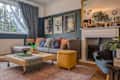 Cozy living room with a gray sofa, colorful cushions, a yellow ottoman, and a fireplace, featuring artwork and plants.