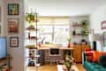 Cozy home office with a wooden desk, black chair, plants, and colorful decor, featuring bookshelves and a green sofa.